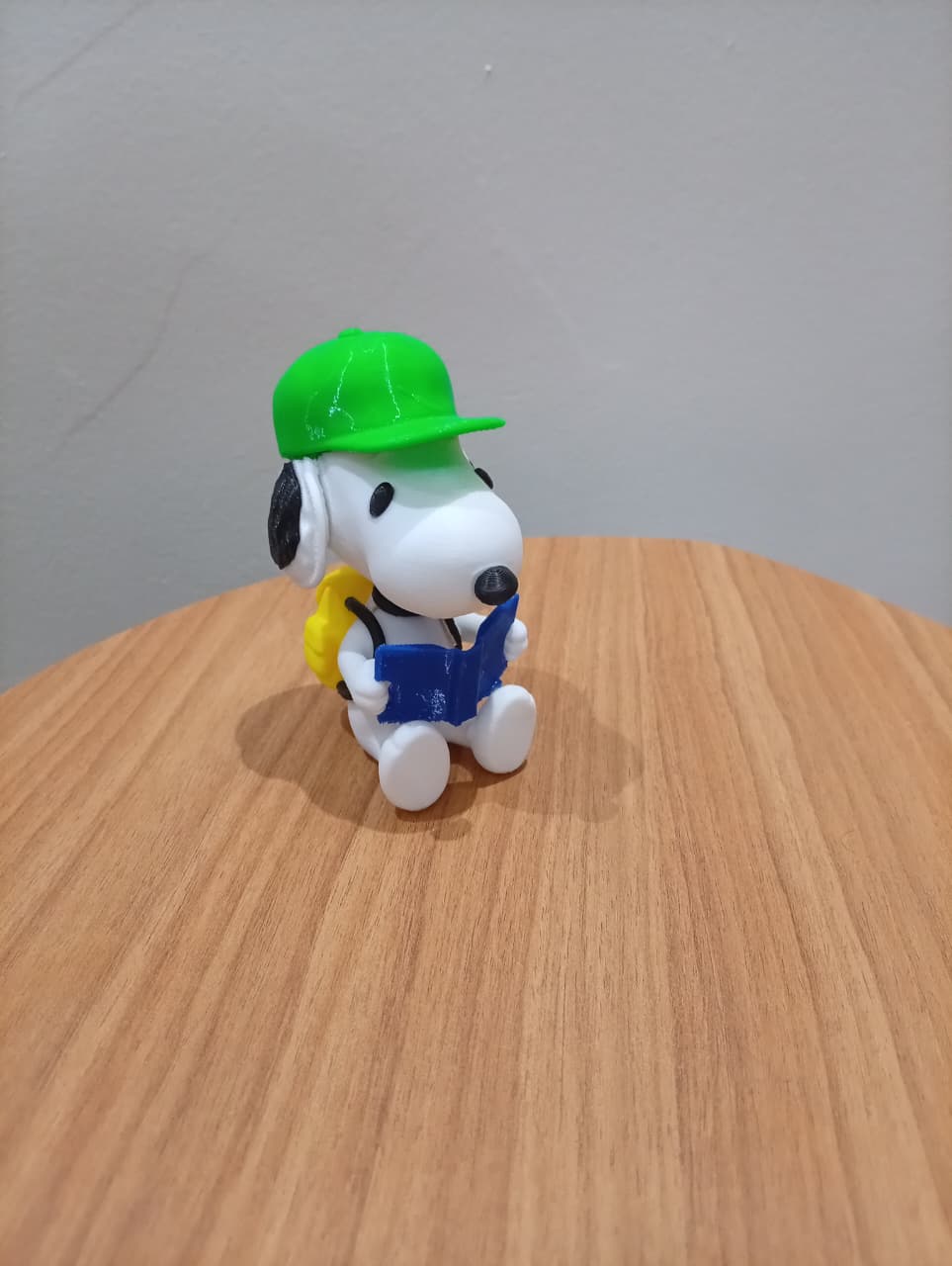 Snoopy decorativo com boné verde e livro azul, visto de frente